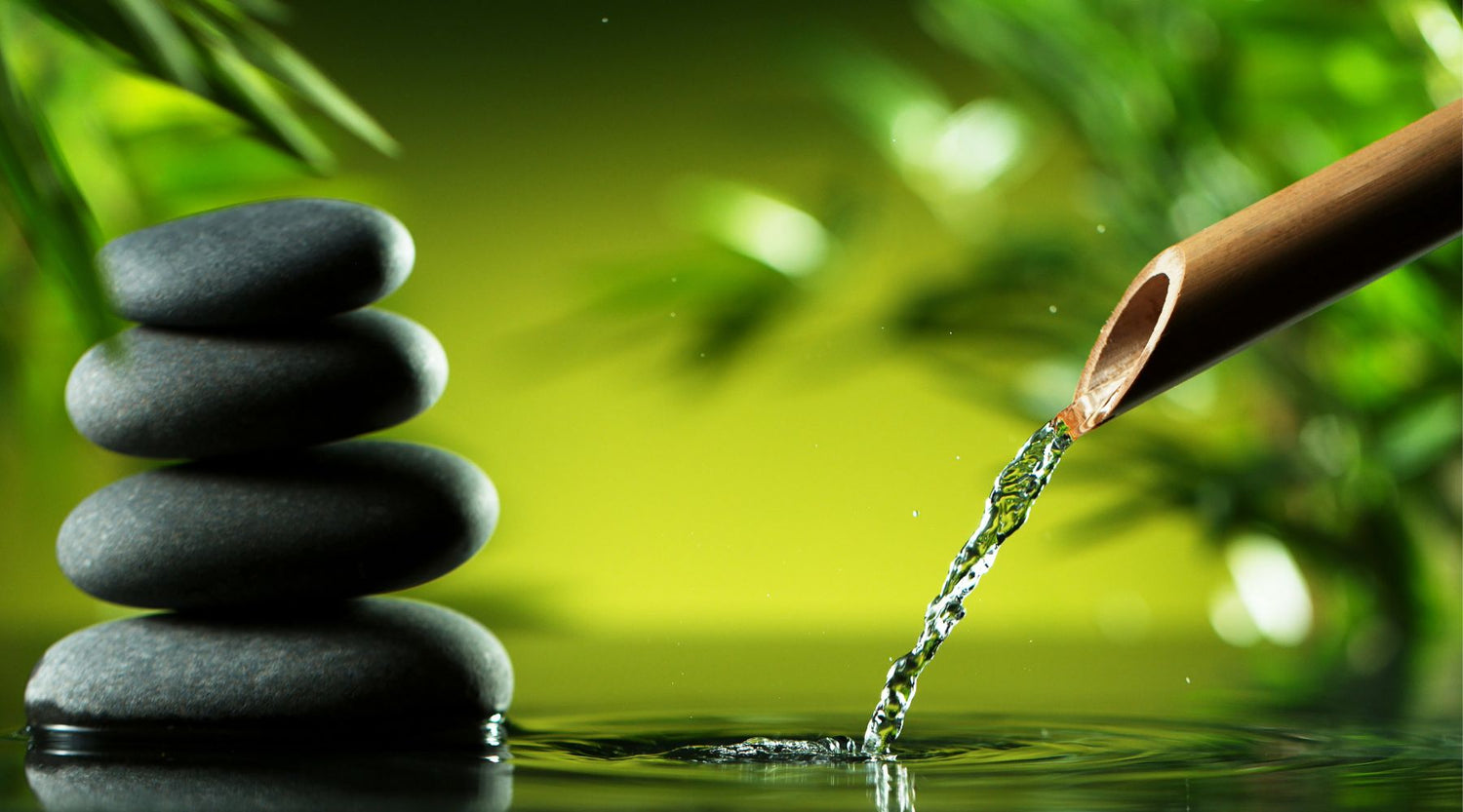 Water flowing through a bamboo pipe on to a calm pool with rock cairns.