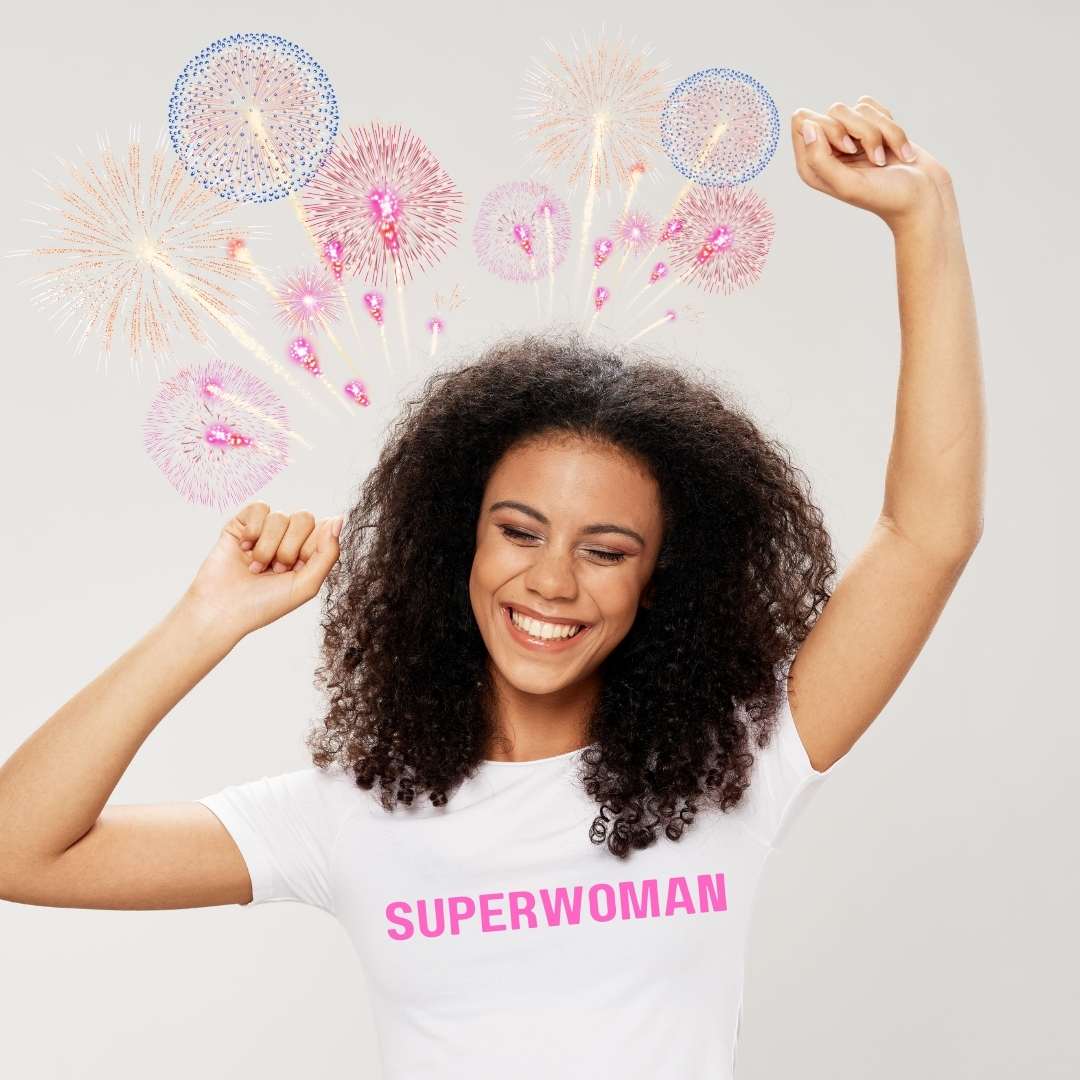 Young woman in superwoman t shirt cheering with fireworks going off overhead.